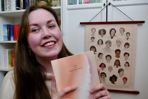 Milena's is holding a notebook with the A-Z female author posted on the bookshelves behind her